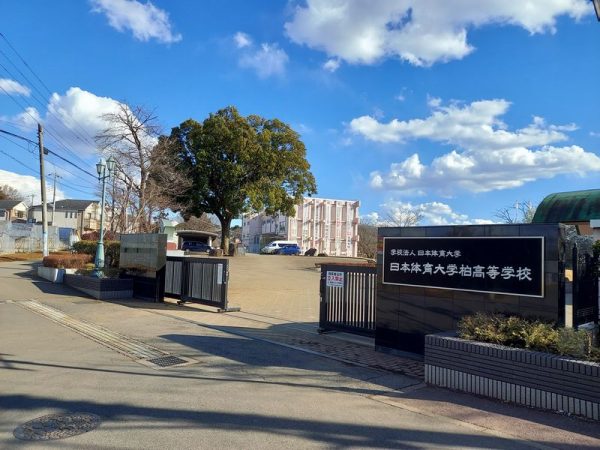 日体高校の正門左側の道に沿っていきます。（正門と反対側の道に「戸張地区公園」の看板も立っています。）