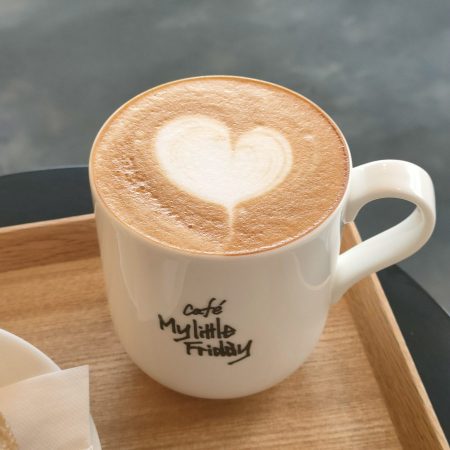 お店のロゴが入ったマグカップに、ハートのラテアートがかわいらしいカフェラテ