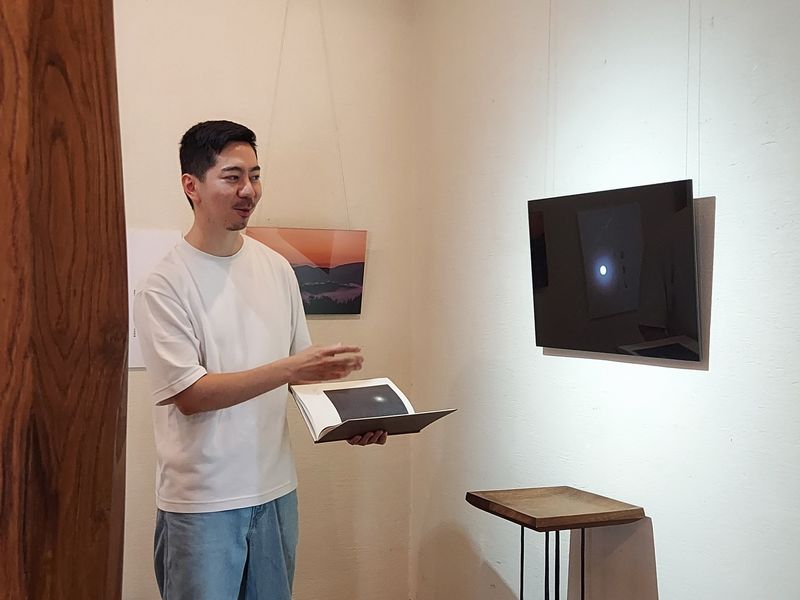 美術館に置いてあった野十郎の図録を片手に、月山（がっさん）で撮影した作品について説明してくださる晃希さん。