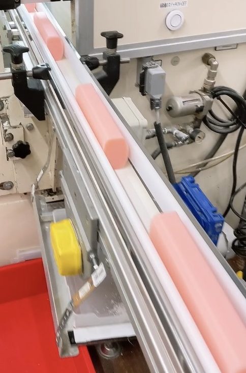 専用白衣を着用　髪の毛など防止のためダストクリーナーをして　工場へ　石けんの原型が　流れている　＊画像は施設提供