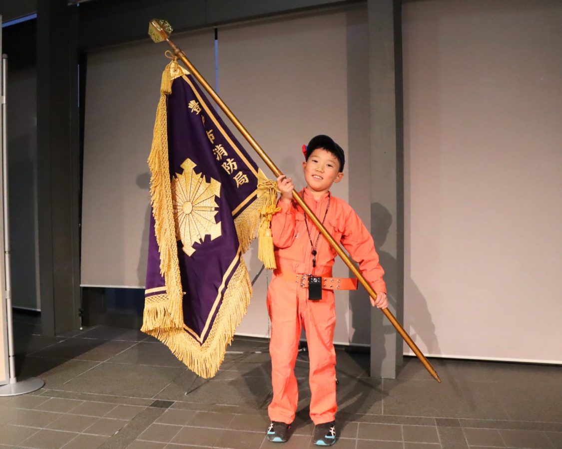 なんと！特別に豊中市消防局の旗を持たせてもらいました。「重たいけど、大丈夫！」と笑顔いっぱい！