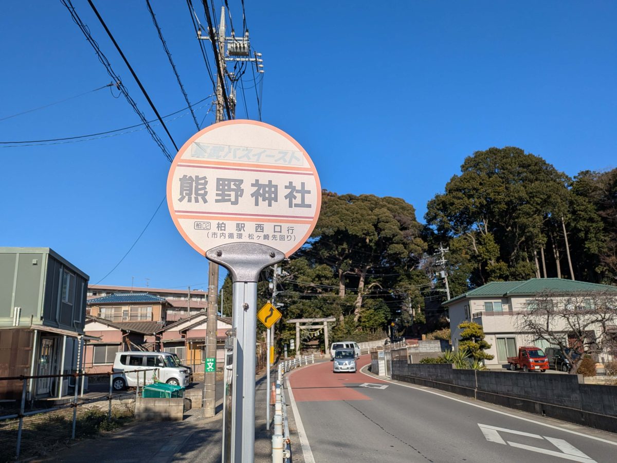 熊野神社バス停。写真奥に熊野神社の鎮守の杜や鳥居が見えます。